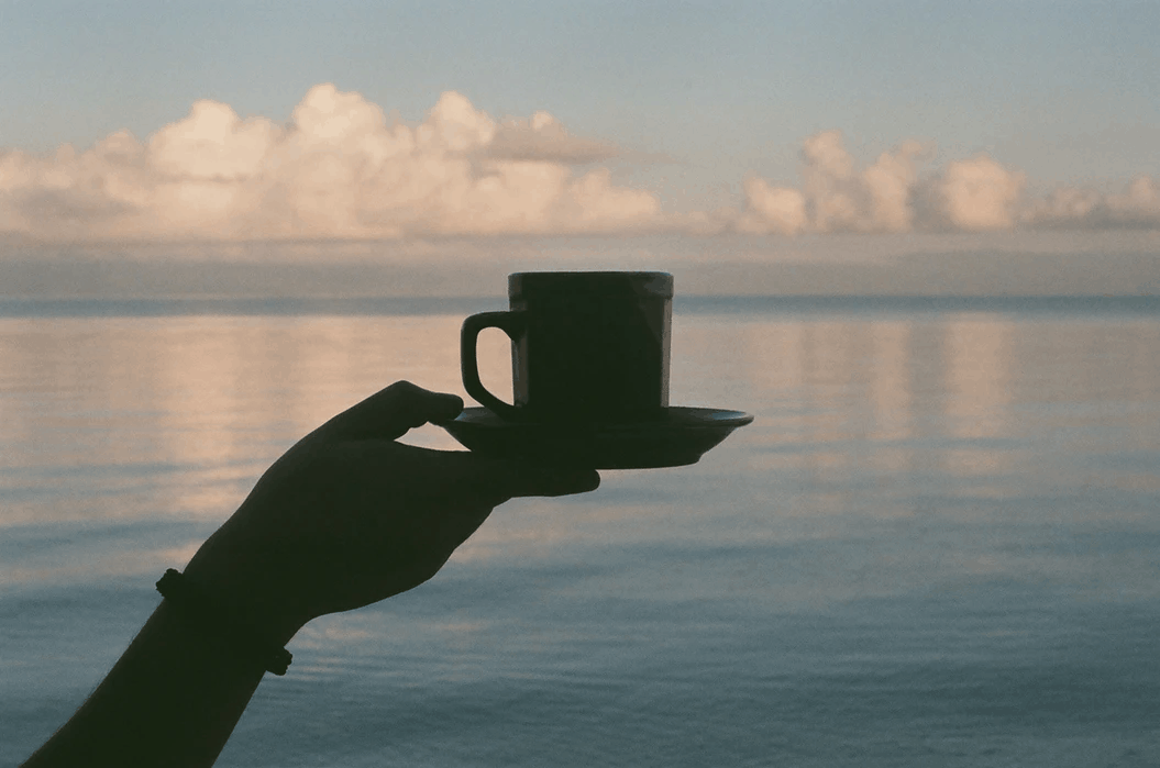 arm holding a coffee mug in front of ocean