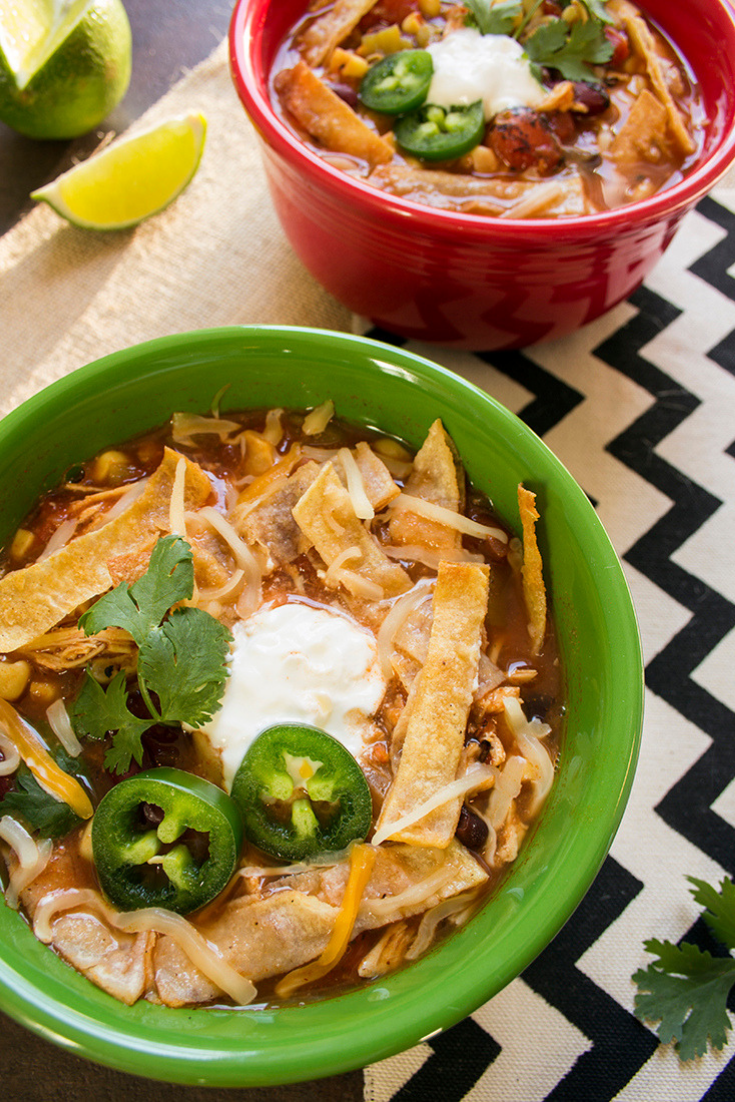 Two bowls of chicken tortilla soup on the counter with tortilla strips and jalapeno