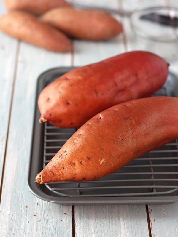 Two sweet potatoes are oiled on a pan