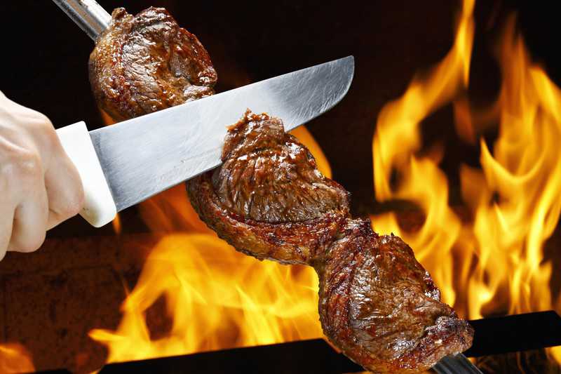 Roast beef or culotte steak on long metal skewers near the fire