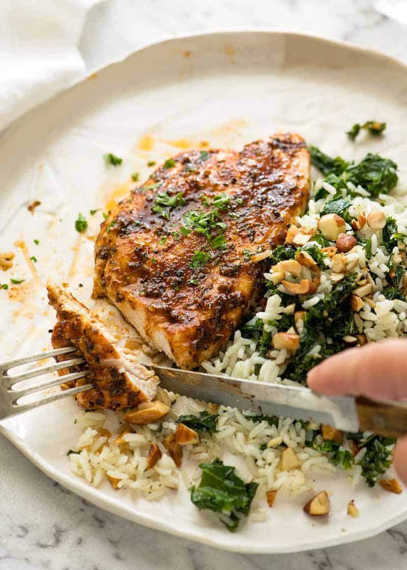 Juicy oven-roasted chicken breast on a white plate with garlic butter rice with kale