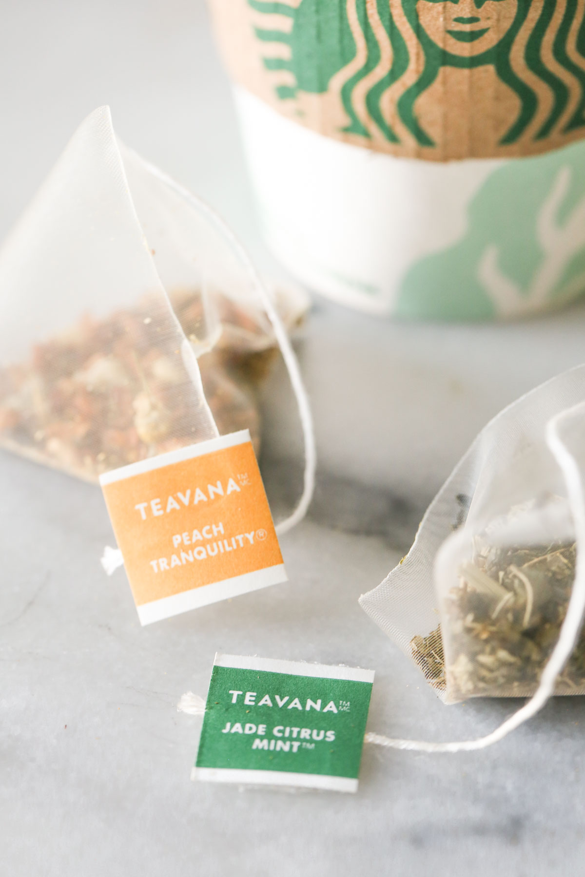 Close-up shot of a Teavana Peach Tranquility tea pack next to a Teavana Jade Citrus Mint tea pack, with a Starbucks cup in the background.