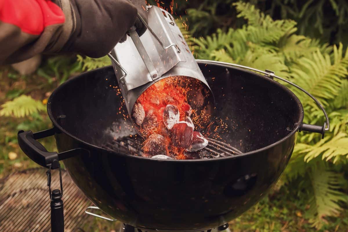 A man pouring lit coals from a chimney starter into a charcoal grill