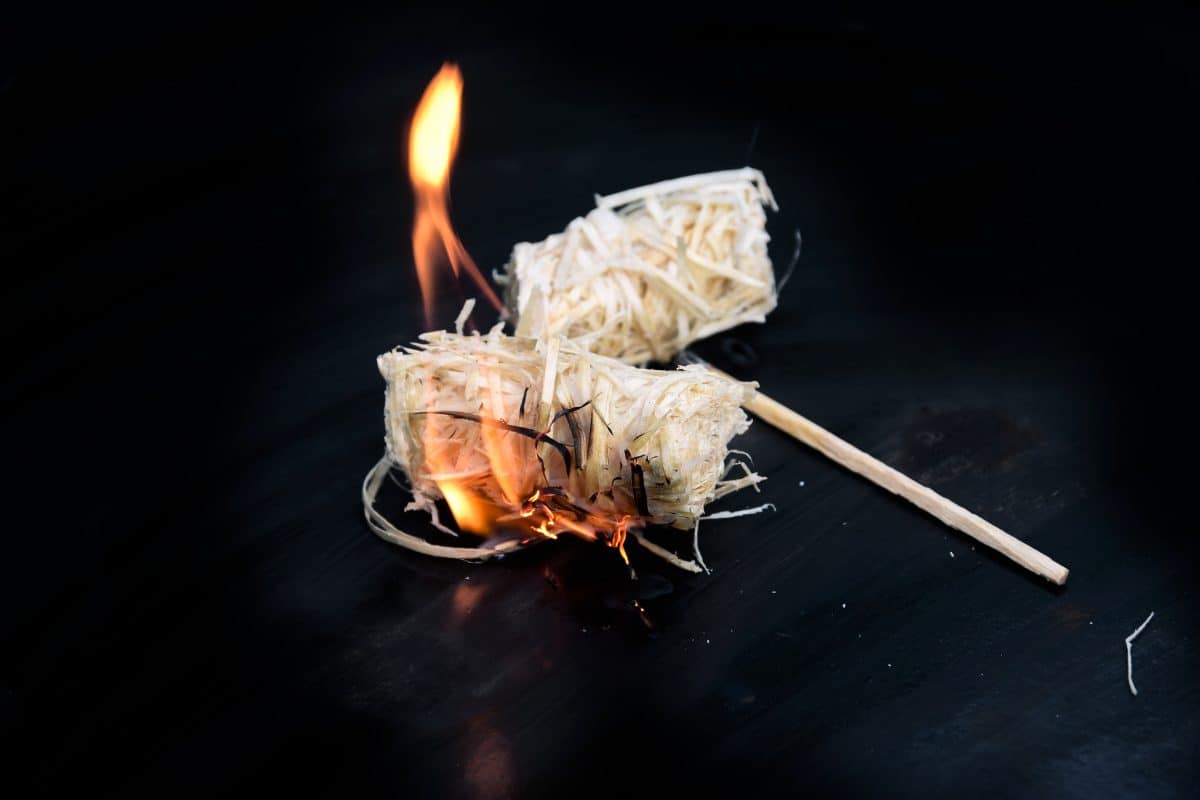Two lit natural wood wool and wax firelighters on a dark background