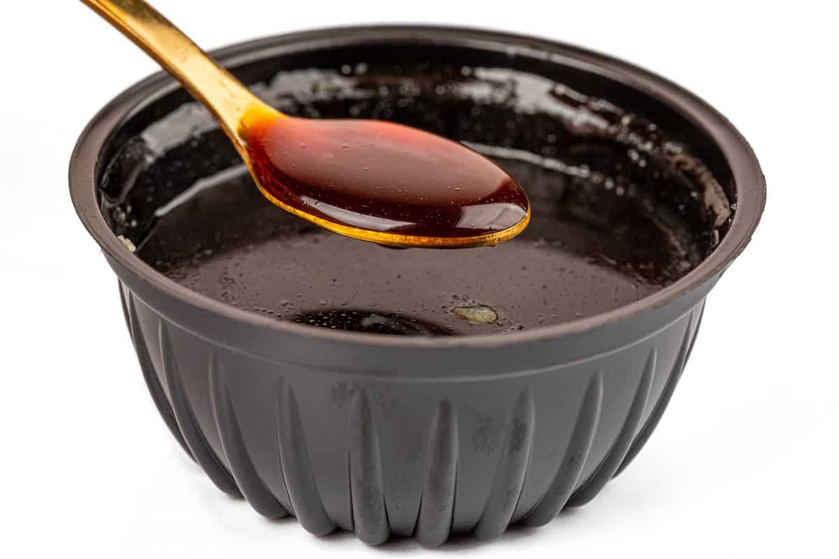 A spoonful of thick BBQ sauce, above a bowl of it, isolated on white