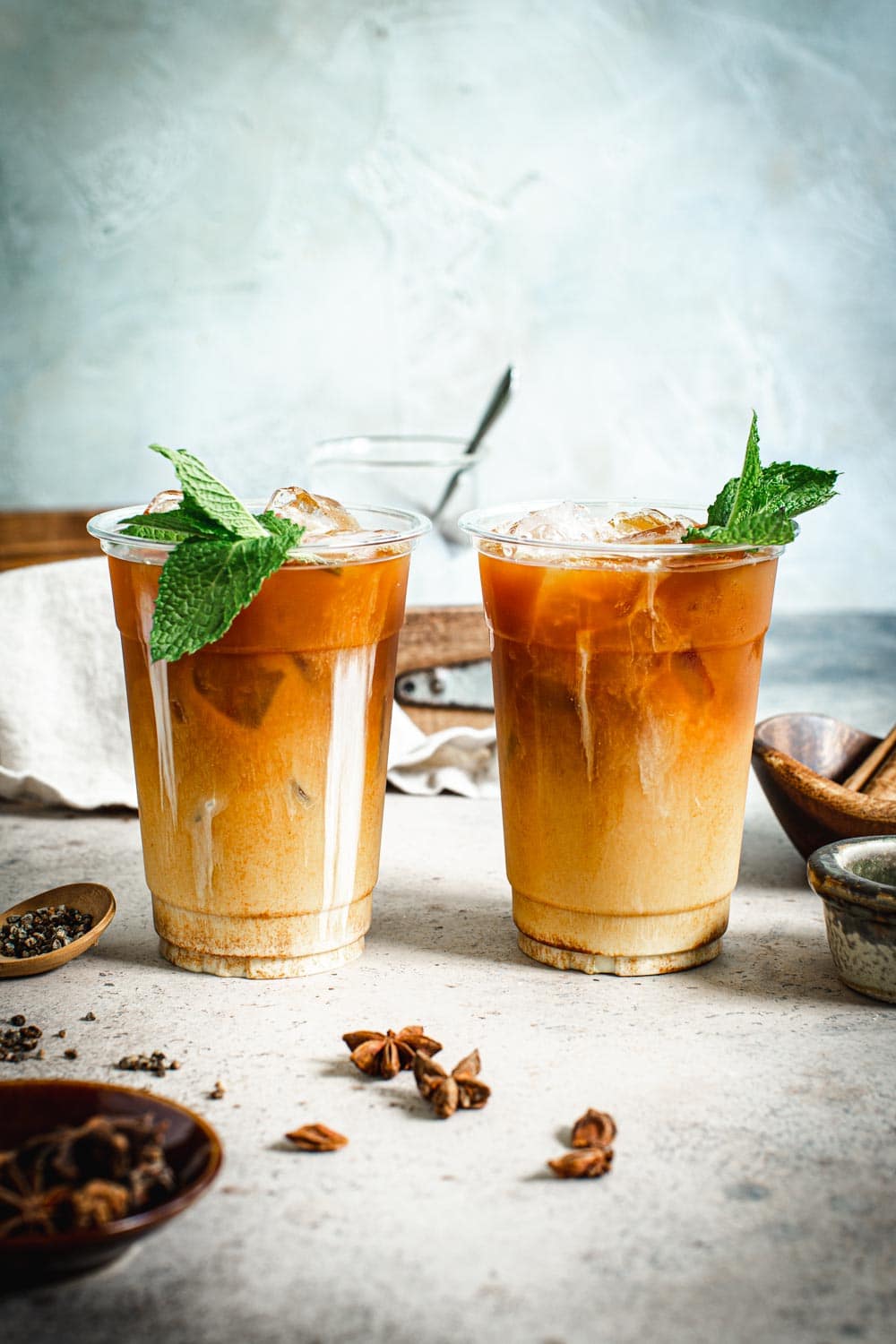 two cups of Thai iced tea with mint leaves and all the spices around