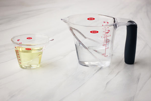 A mini measuring cup with oil and a 1-cup measuring cup with water.