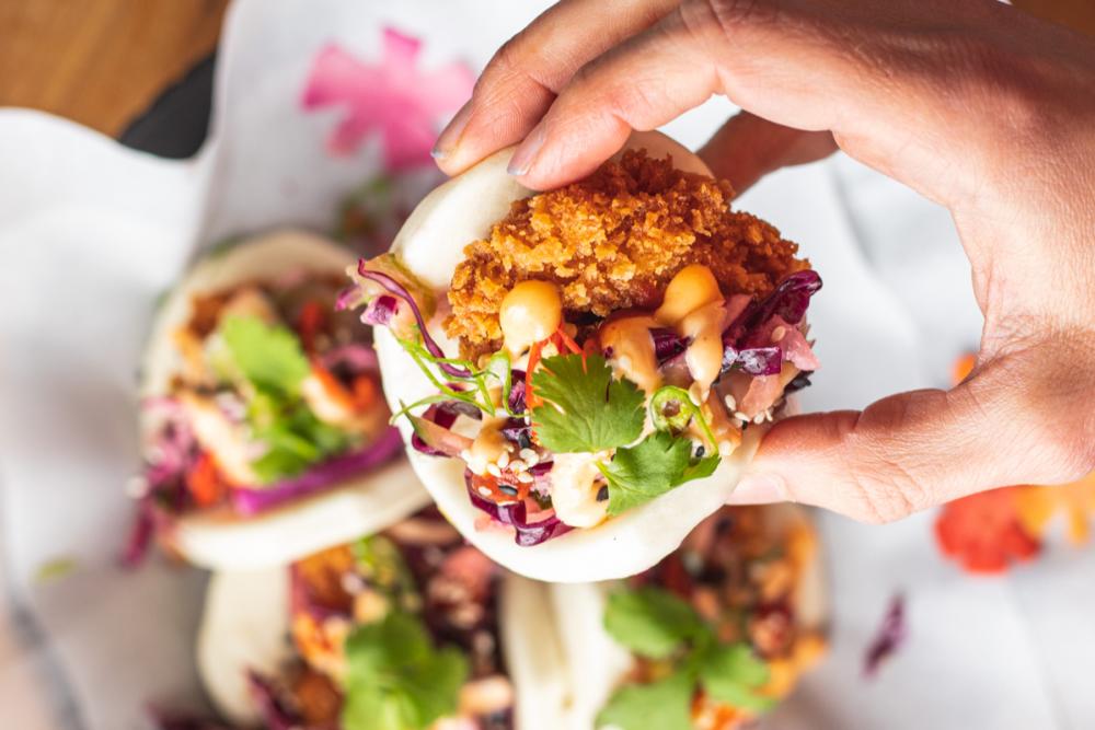 photo of Plow Bao's hand holding a taco bag with fried chicken, cabbage, cilantro and sauce