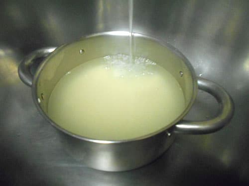 Water from the faucet flows into a stainless steel pan filled with rice