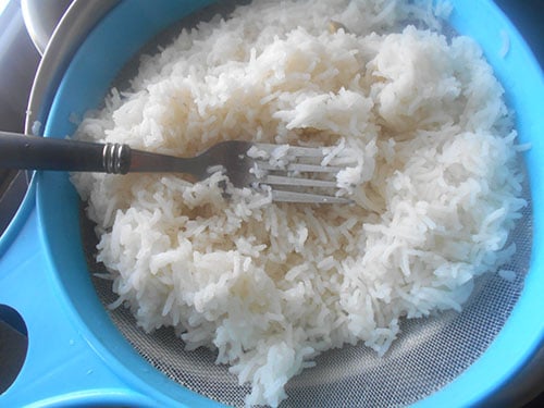 Top view of cooked rice in a nylon sieve with a fork on top