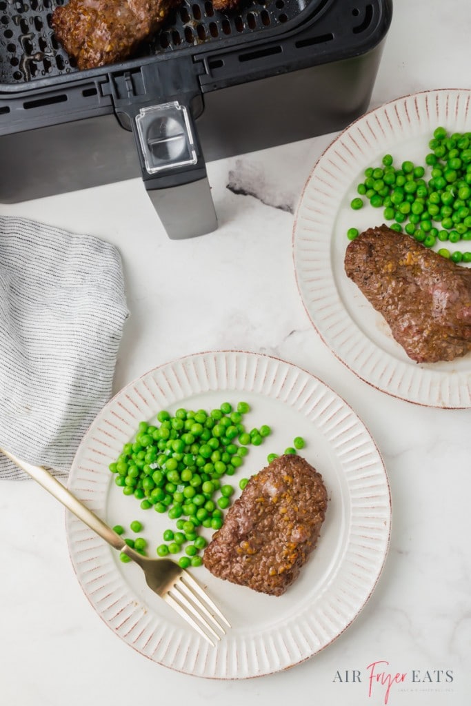 two cubes of steak and peas next to an air fryer.
