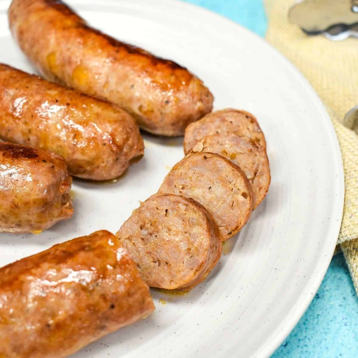 Close-up image of sausage served on a white plate. A portion of a sausage cut into bite-sized pieces.
