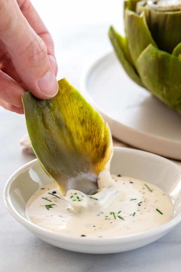 person holding artichoke leaves in white dipping sauce