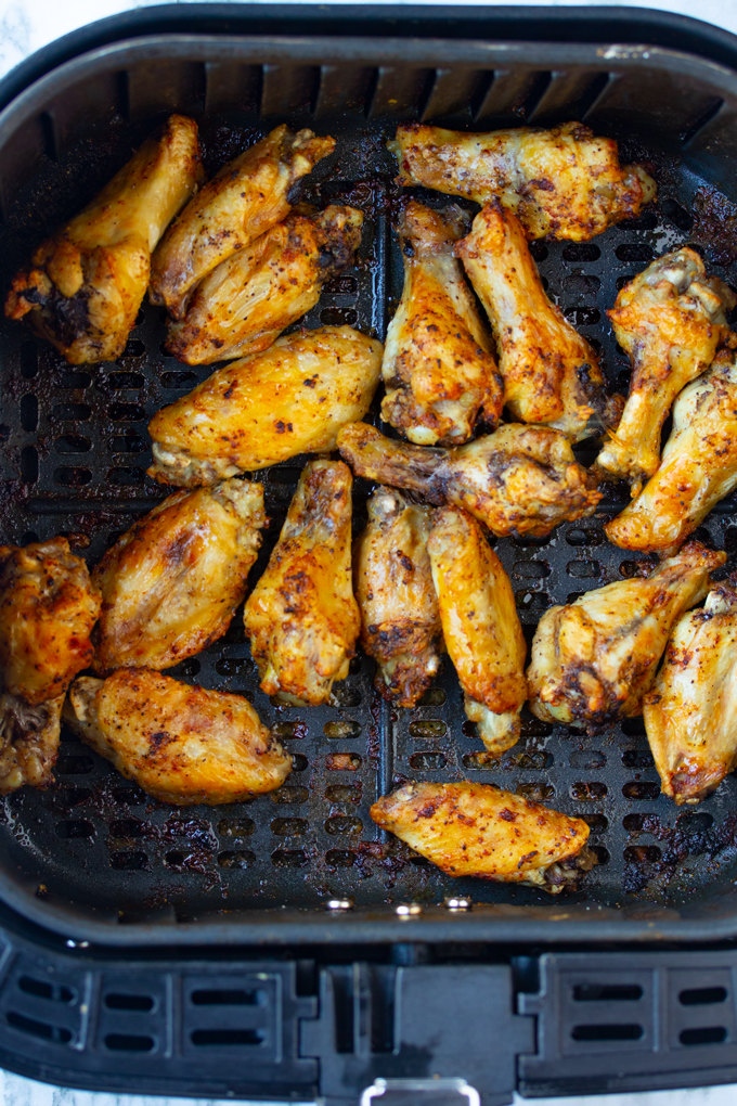 cooked chicken wings in air fryer basket with spices in it