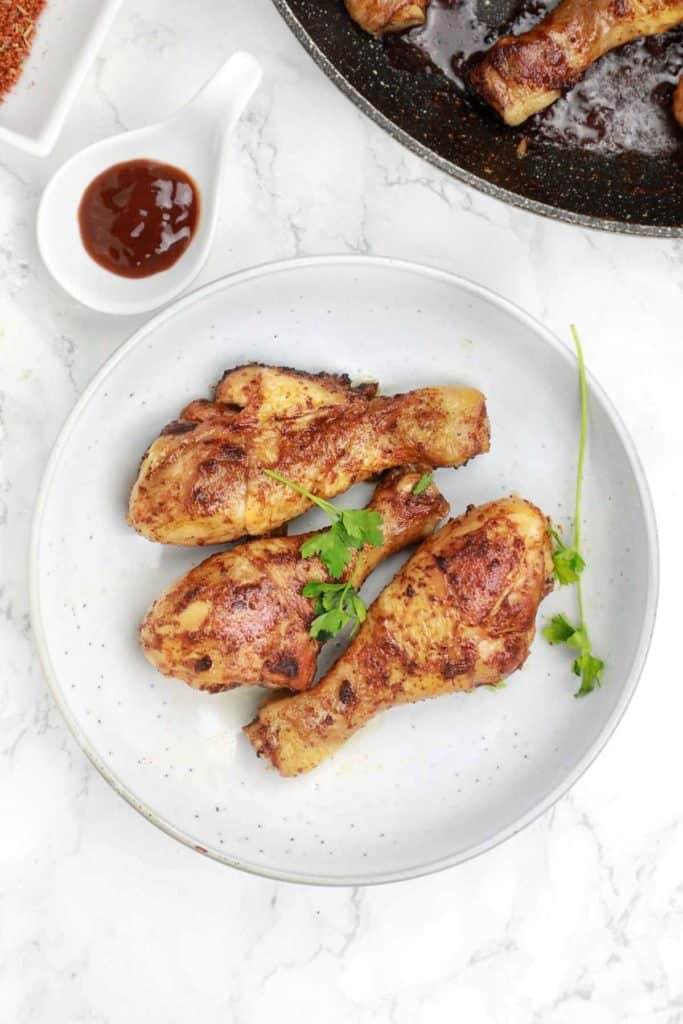 Serve the cooked chicken in a plate with the pan on the background.