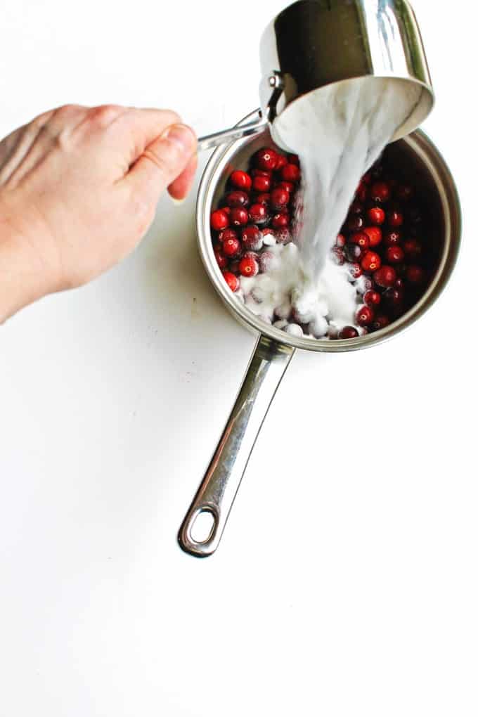 sugar is poured into cranberries in a pot