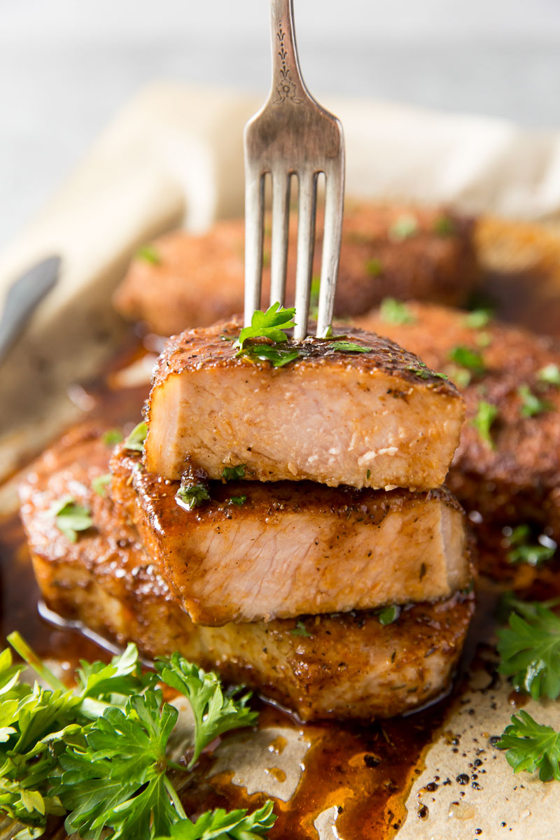 Juicy cooked pork chops stacked, with a fork