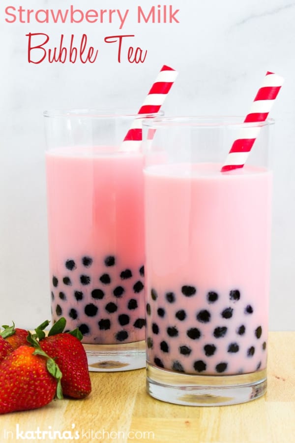 two glasses of strawberry pearl milk tea with black sugar pearls, fresh strawberries and red striped straws
