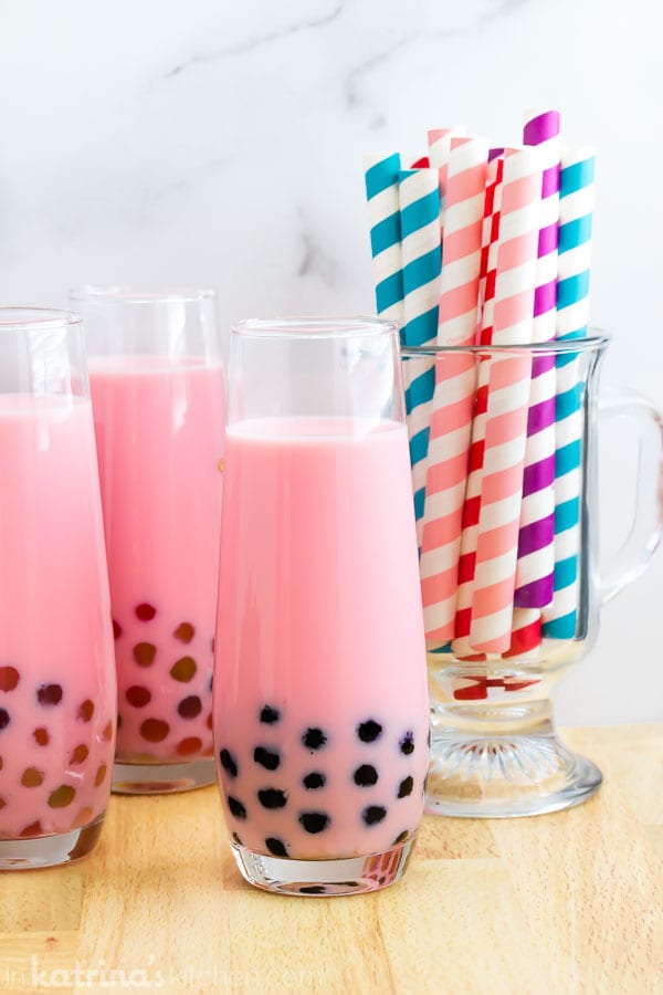 multiple cups of strawberry bubble tea with tapioca pearls and a colorful striped coffee