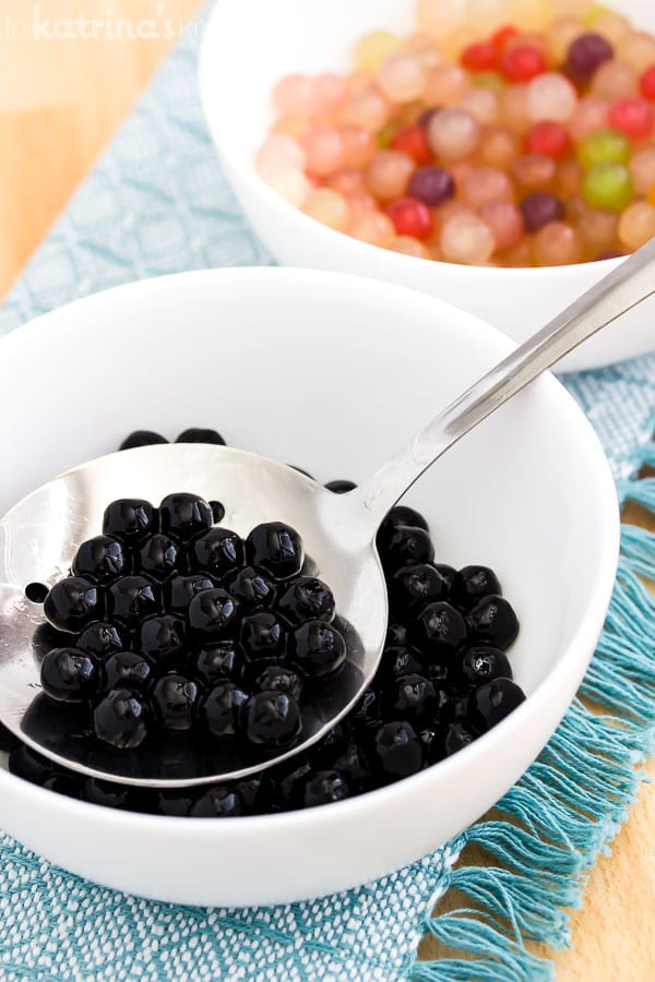 Black tapioca pearls cooked in a slotted spoon scooped from a white bowl