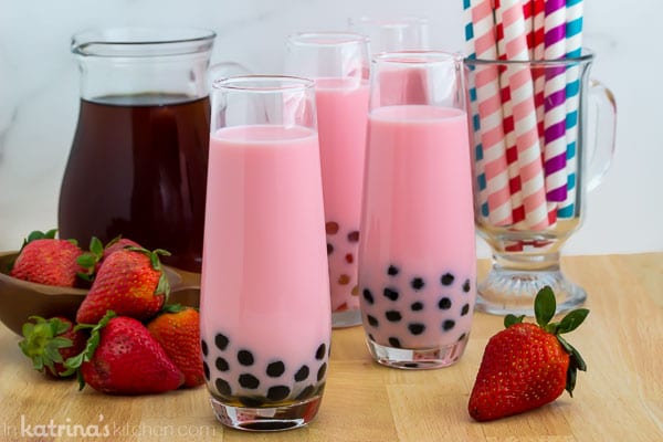 cup of pink strawberry milk tea with tapioca pearls with fresh strawberries, iced tea and a cup of colorful striped straws