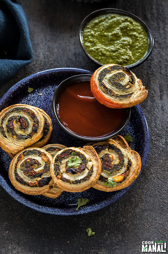 Puffy pinwheels in a blue plate with a bowl of black ketchup
