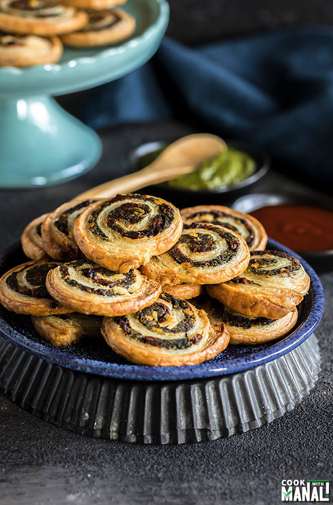 baking pinwheel tomato & spinach & sun-dried tomatoes stacked on blue plate with black bowl topped with chutney and ketchup on background