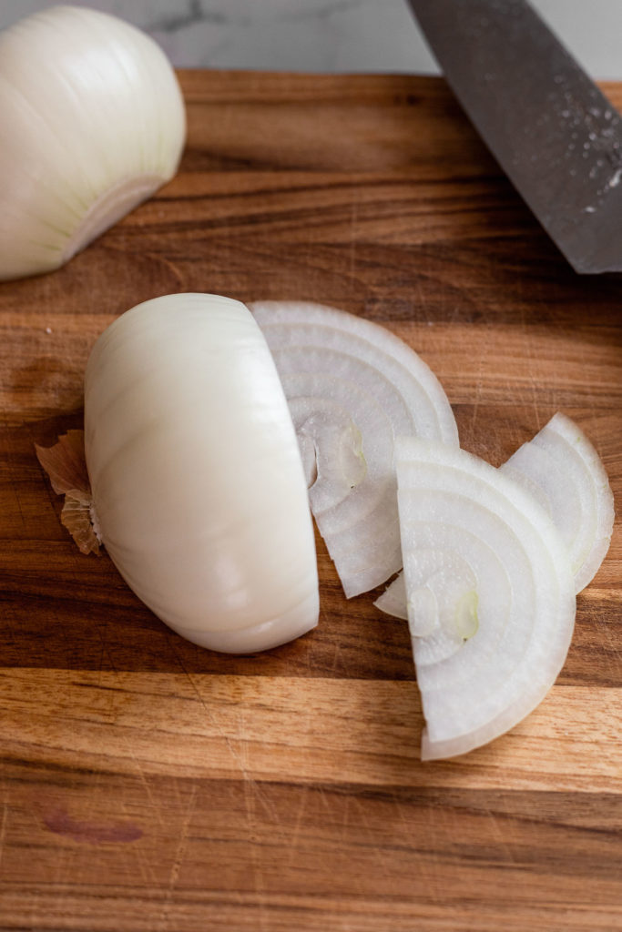 Onions are placed on a cutting board, thinly sliced.