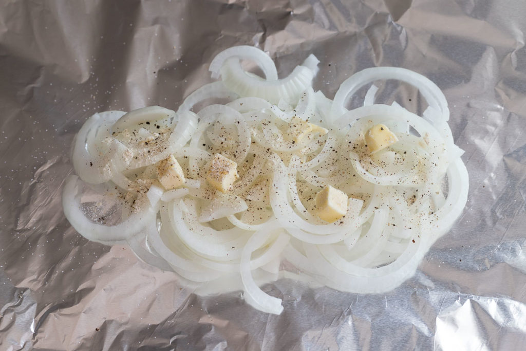 Sliced ​​onion in foil topped with seasoning and butter.