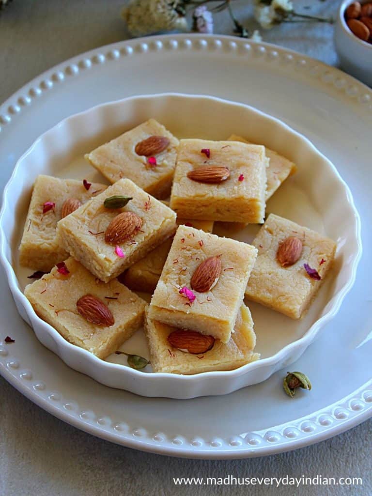 ricotta badam cheese burfi served on a white plate decorated with almonds and rose petals