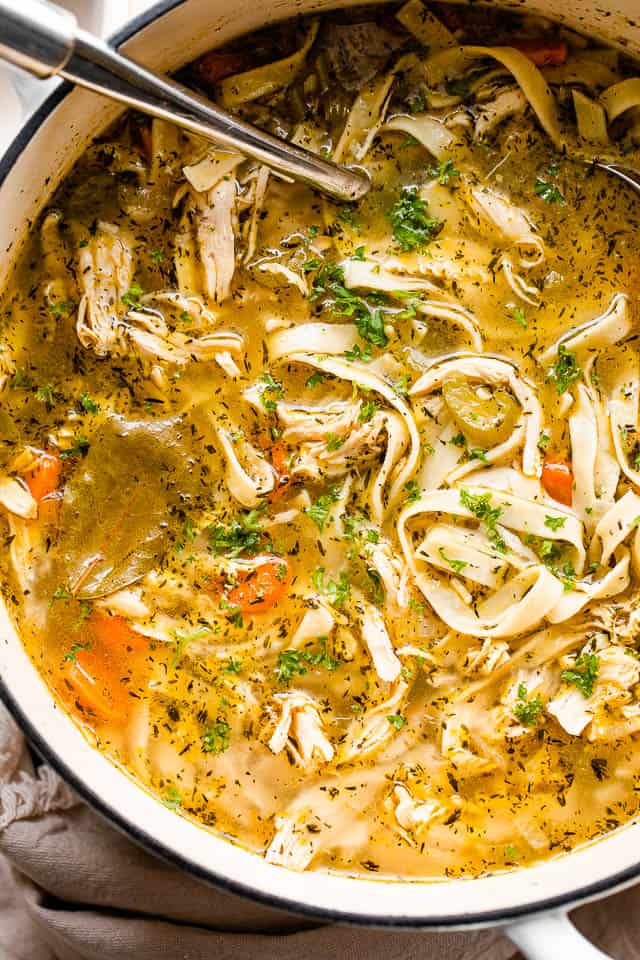 An overhead shot of chicken noodle soup in a white Dutch oven