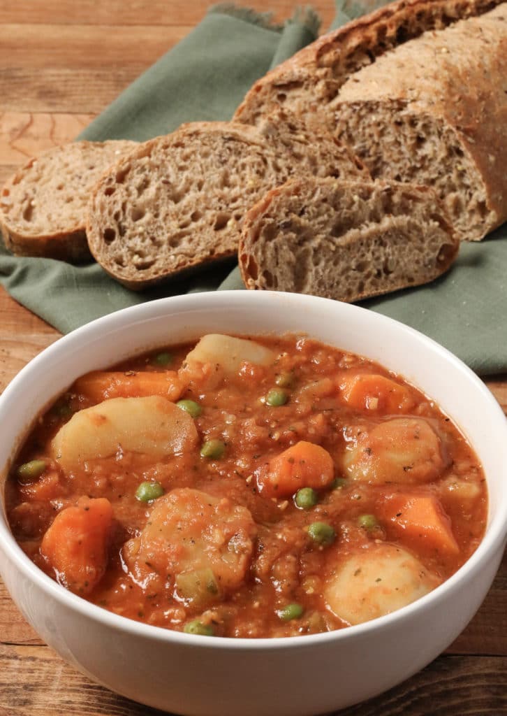 Bowl of Instant Vegetable Stew in a white bowl, placed on a wooden surface, the background is sliced ​​whole grain bread