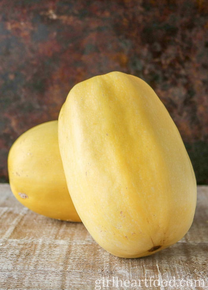 Two uncooked spaghetti squash on a wooden board.