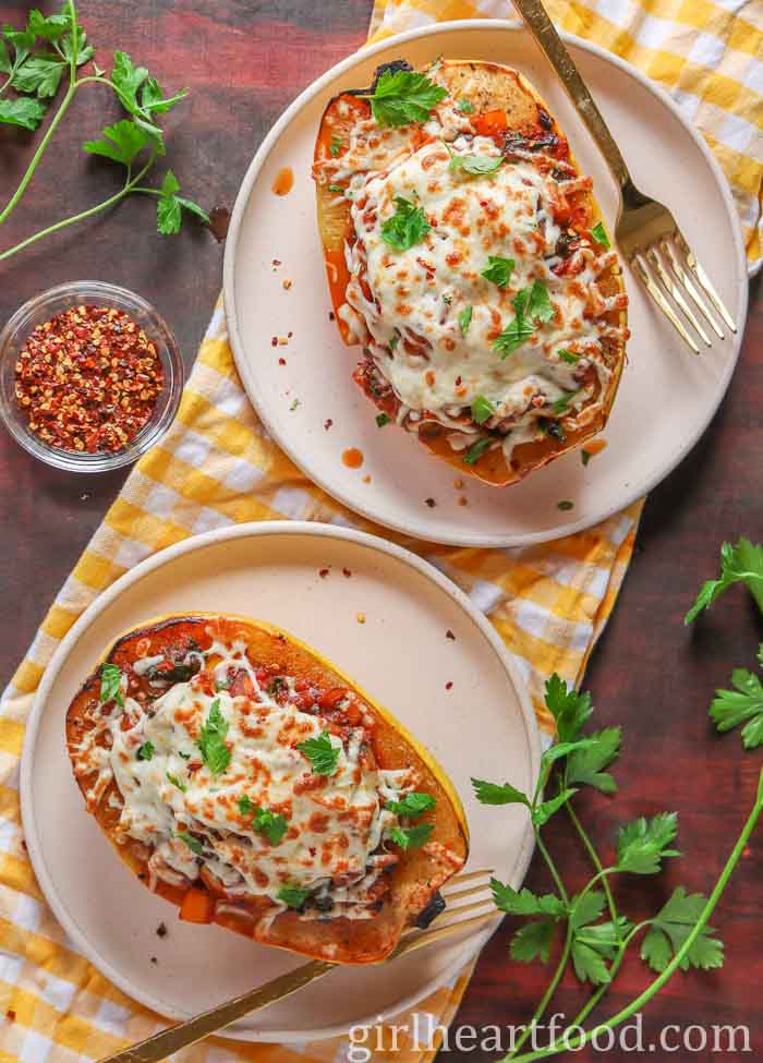 Two pumpkin vessels stuffed with cheese spaghetti, each vessel on a plate with a fork.
