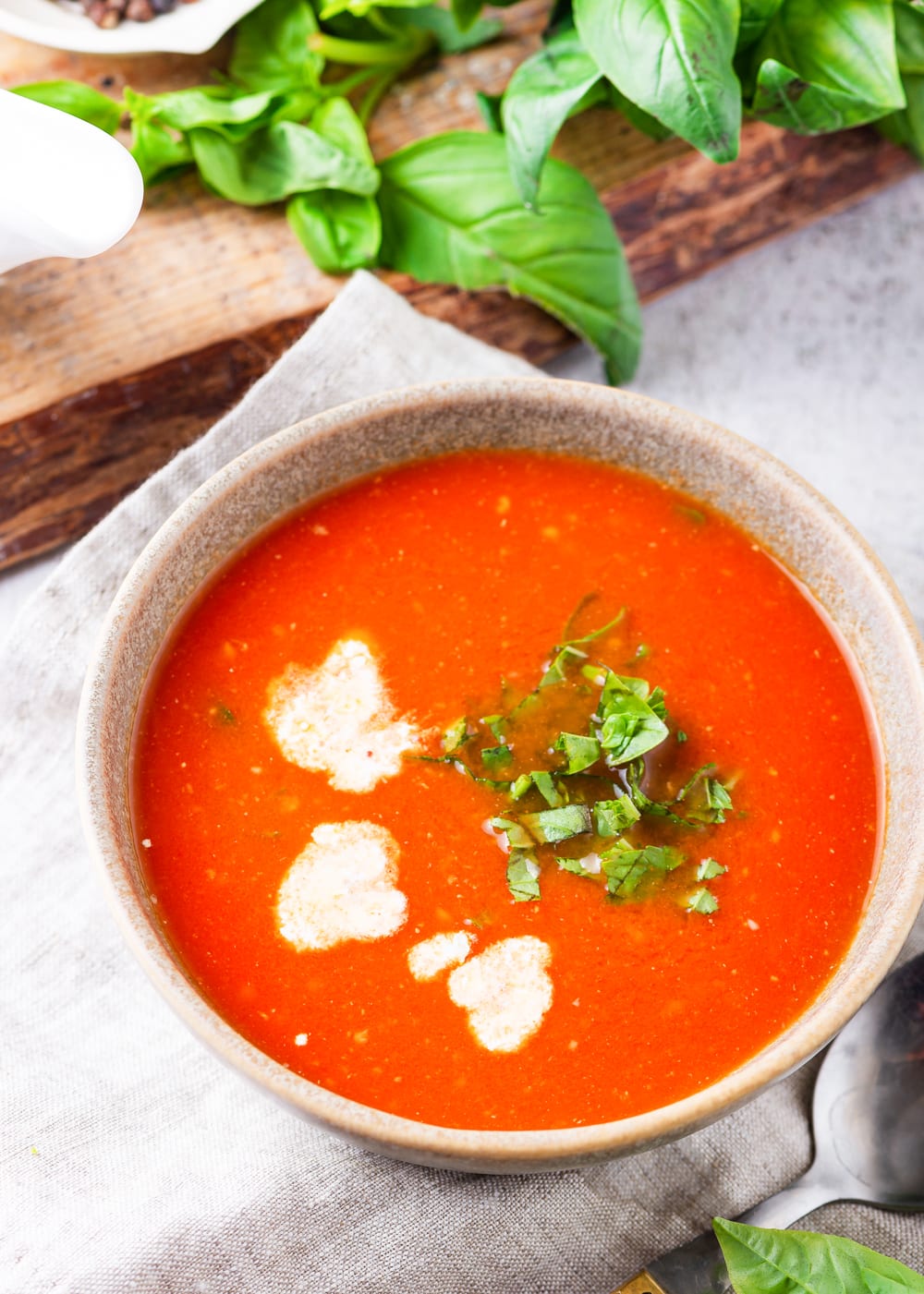 Tomato soup in a bowl with extra cream and chopped basil.