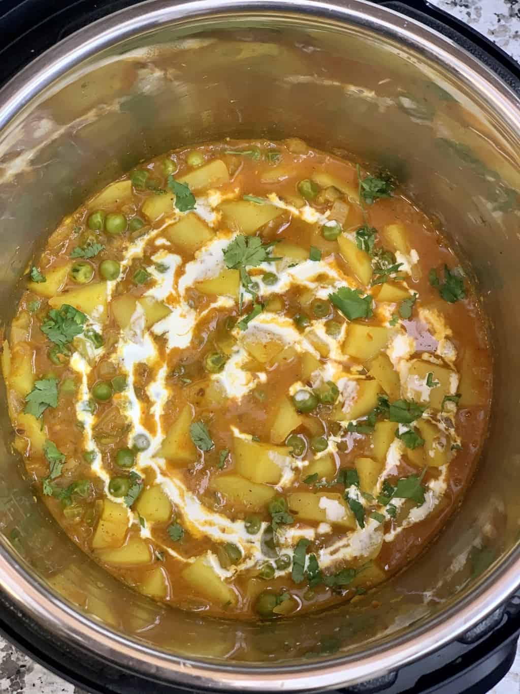 matar aloo in instant pot garnished with cashew cream and cilantro