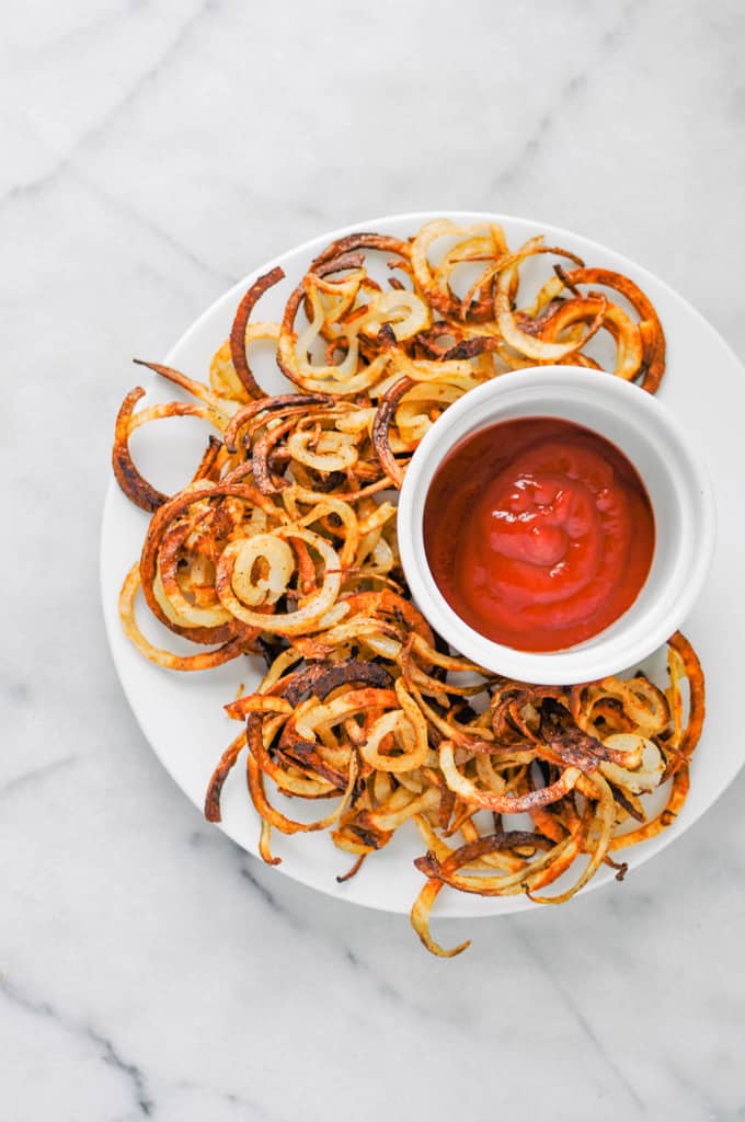 curly fries on a white plate with a bowl of ketchup on a marble countertop