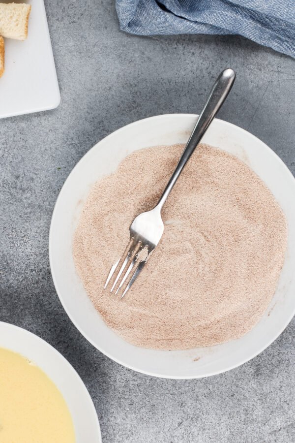 Cinnamon sugar in a white bowl using a fork.
