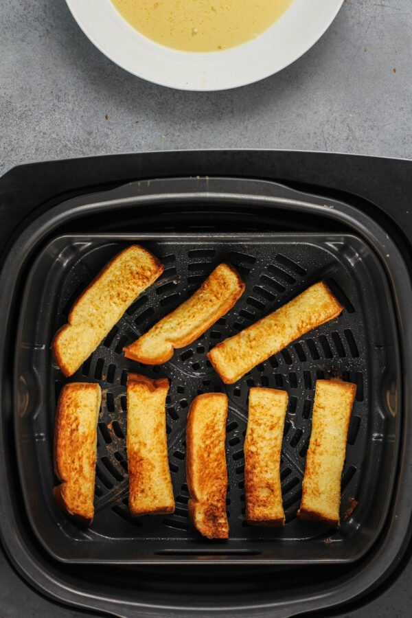 The French toast is fully cooked in the basket of an air fryer.