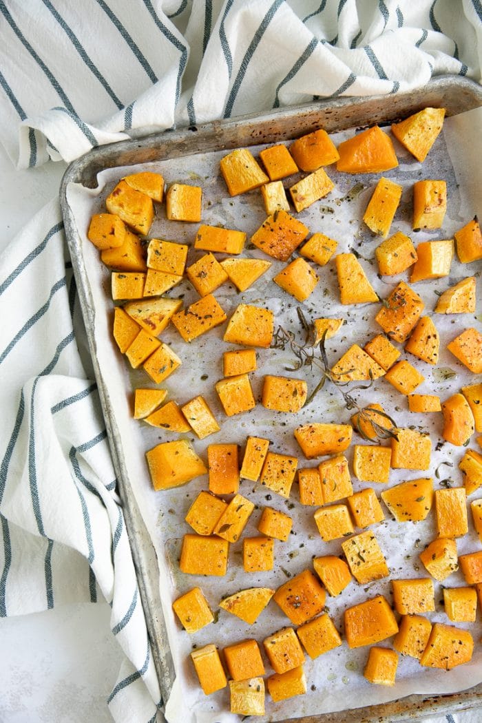 Roast the pumpkin chunks on a large, single-layer baking tray spiced with fresh herbs.