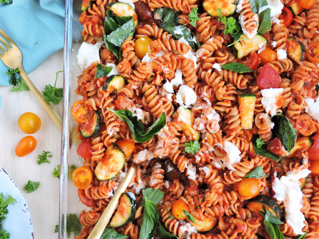Whole Wheat Pasta For Grilled Vegetables in a glass dish stewed with basil leaves, ricotta and tomatoes on top