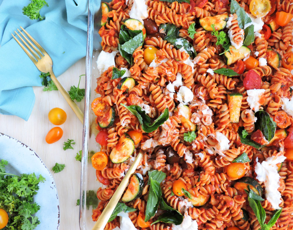Whole Wheat Pasta For Grilled Vegetables in a glass dish stewed with basil leaves, ricotta and tomatoes on top