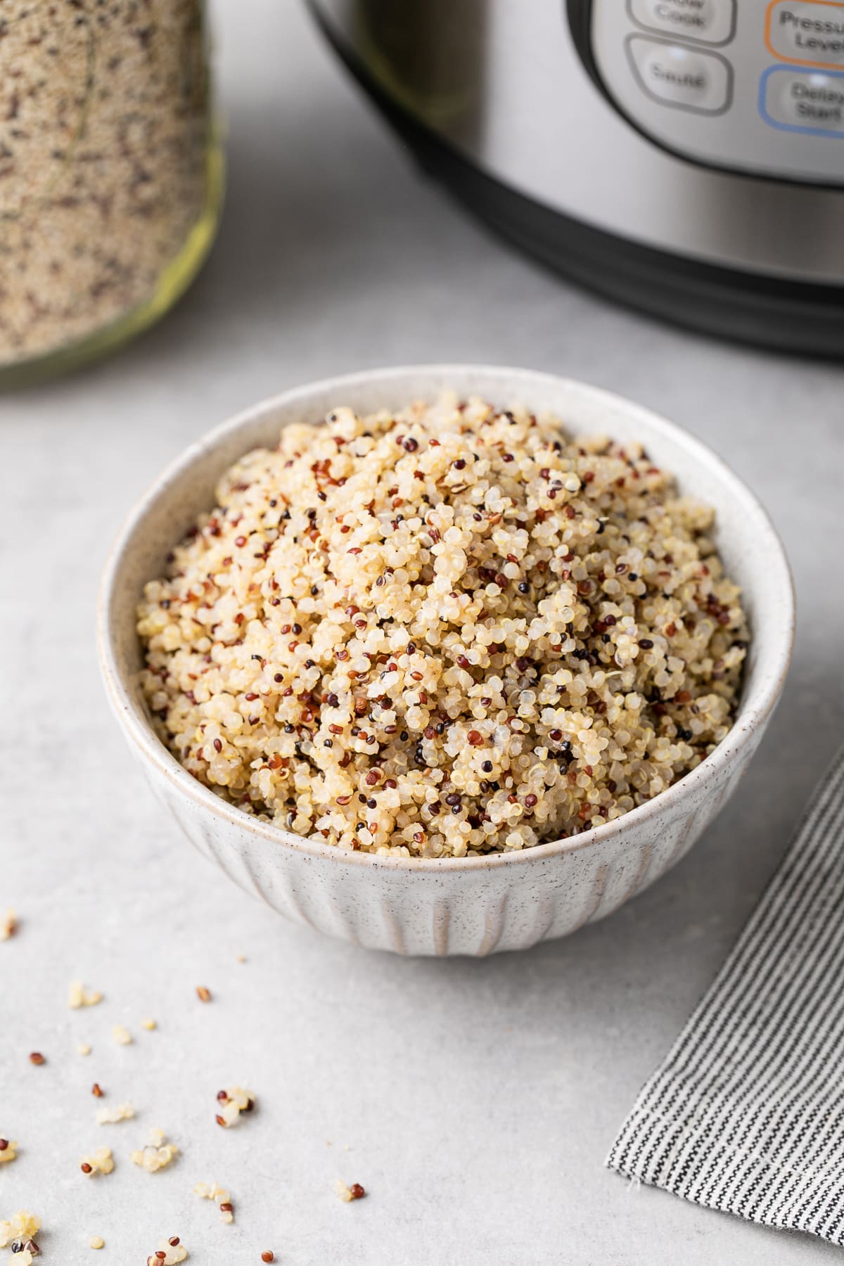 Side view of a bowl filled with quinoa made in a pot with surrounding items.