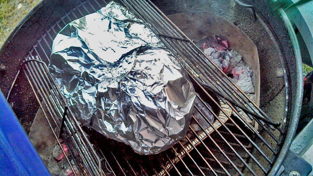 brisket wrapped in aluminum foil on the grill