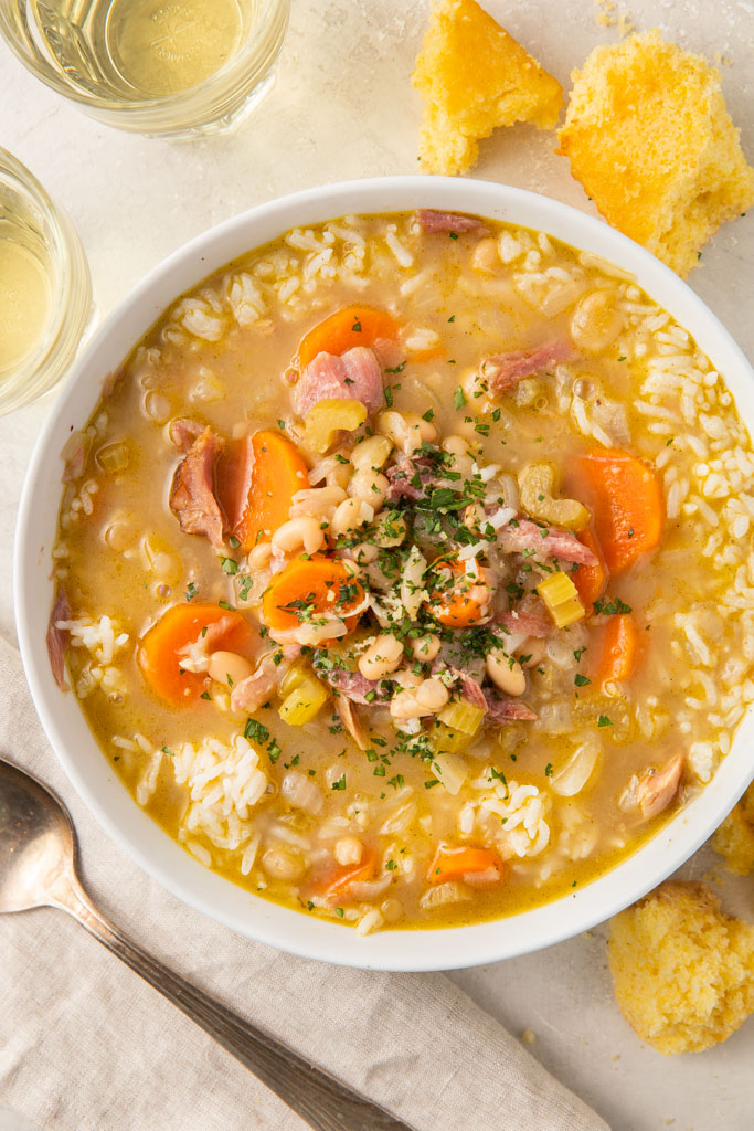 A bowl of smoked turkey soup with carrots, celery and beans on a white table