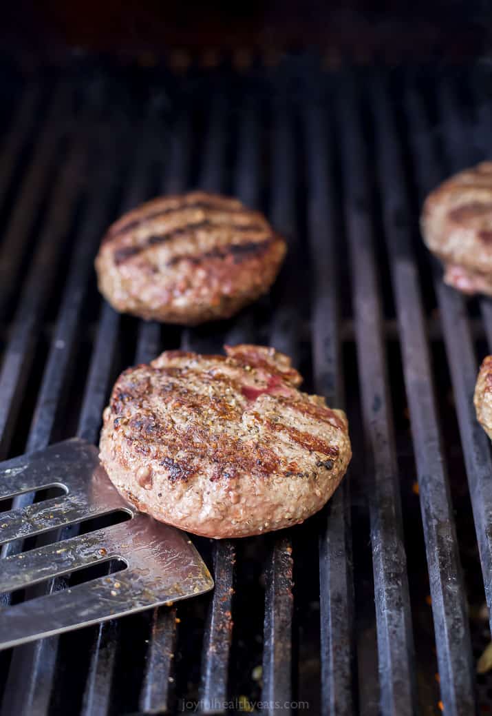 Burgers are grilled on a gas stove with a spoon ready to flip
