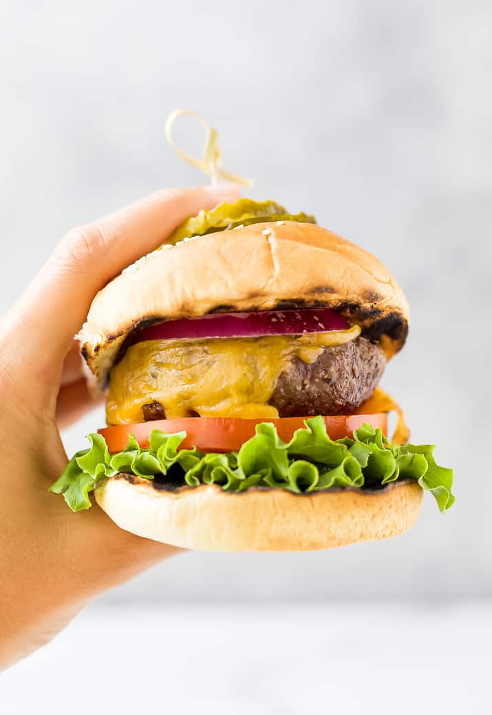 Hand holding the most delicious grilled burger with onions, tomatoes and pickles