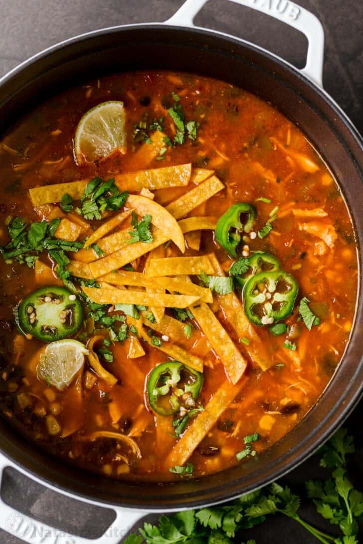 Easy chicken tortilla soup in a pot garnished with tortilla strips, jalapeños, and cilantro