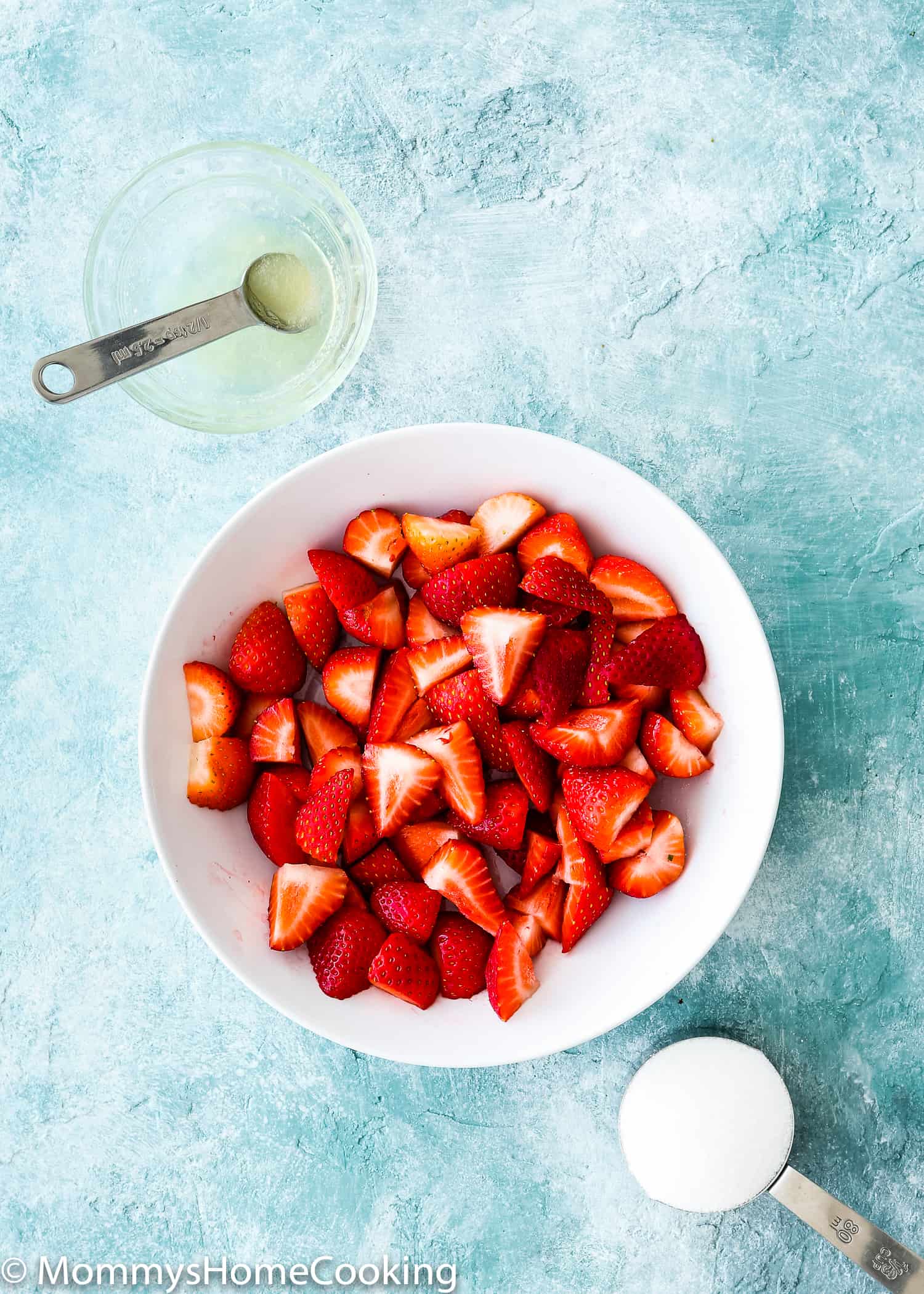 white bowl with chopped strawberries, bowl of lemonade and a cup of sugar