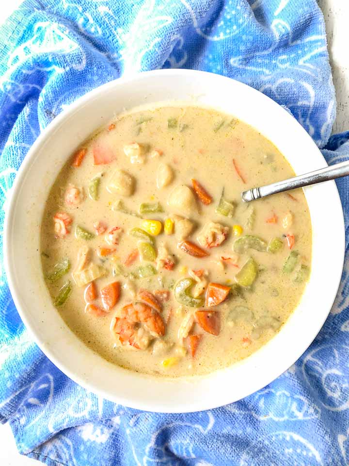 large white bowl of creamy seafood soup with bright blue spatula and towels